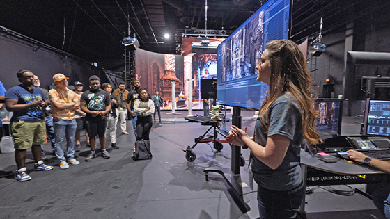 A tour guide shows a large screen displaying a virtual movie set to a group of potential students in Full Sail’s virtual production studio.