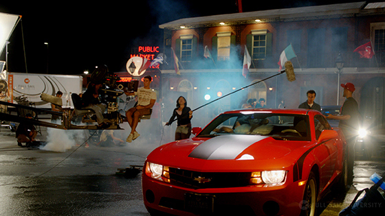 Students hold boom mics and operate cameras around a red sports car as they film a scene on Full Sail’s Backlot.
