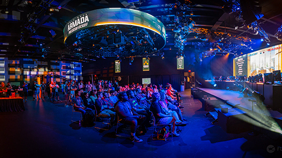 A large audience sits in the Full Sail University Orlando Health Fortress and watches a stage with esports competitors playing on PCs.
