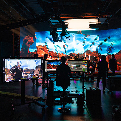 Students work on set in a virtual production studio. A large LED backdrop covers the wall and displays a virtual set of a desert on a distant planet.