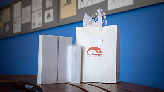 A white bag with the hangr logo and boxes with an Apple laptop and keyboard sit on a table.